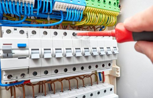 Switchboard with automatic circuit breakers. Dielectric screwdriver in the electrician hand. Background and texture